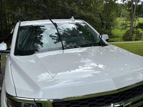 Hood and grille of a white Chevrolet Tahoe after an exterior detail, with trees reflected in the paint