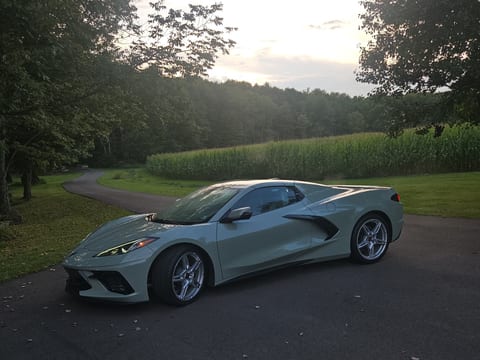 Grey-green Chevrolet Corvette after an exterior detail, parked on a driveway beside a corn field at sunset