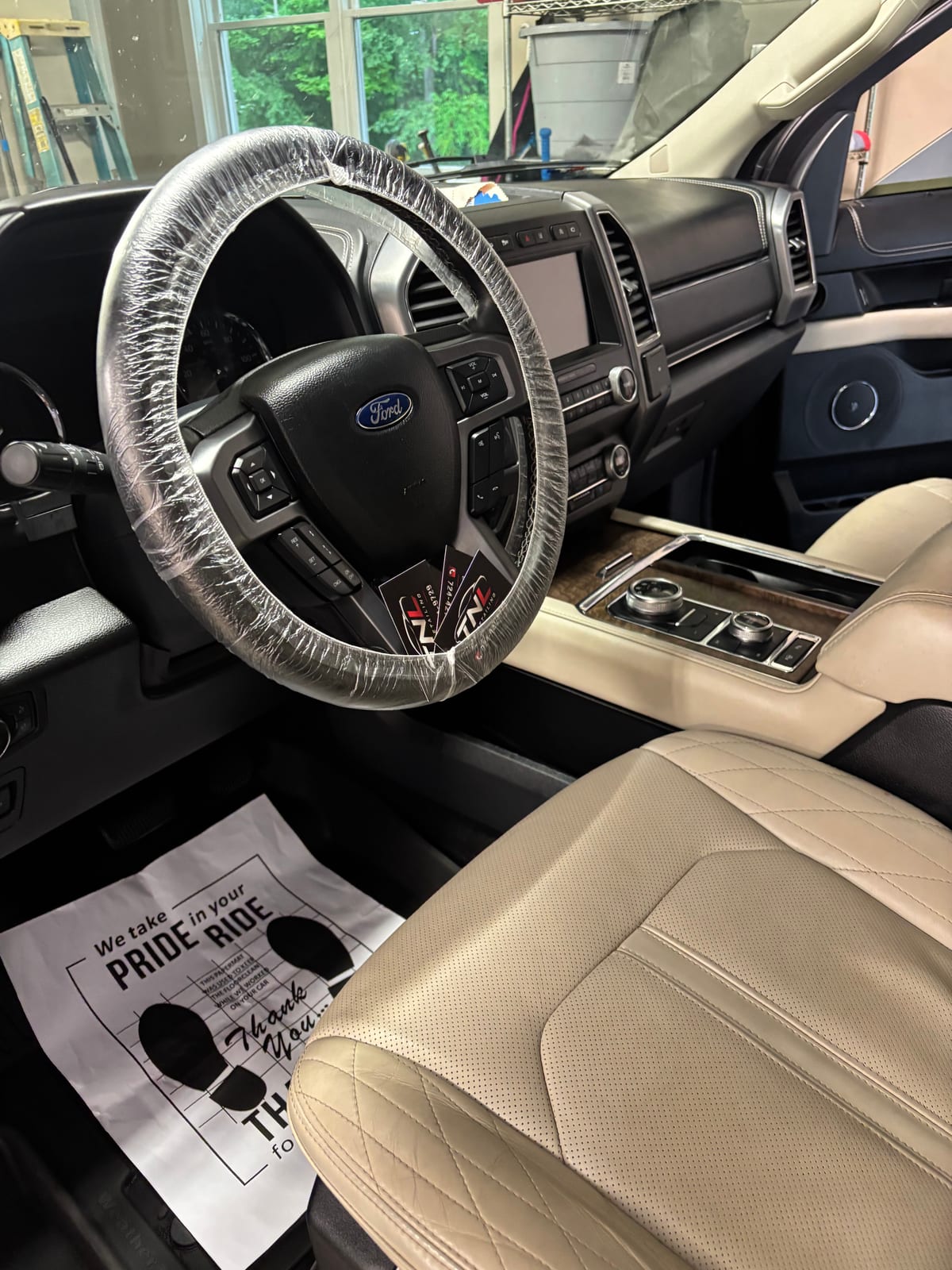 Disposable steering wheel cover in place, with a TNL Detailing paper floor mat and business cards left on the seat of a finished Ford Expedition