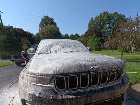 Jeep Grand Cherokee covered in snow foam during an exterior hand wash on a driveway