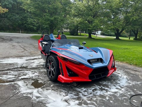Red and blue Polaris Slingshot on a driveway after an exterior hand wash, wash suds still on the pavement around it